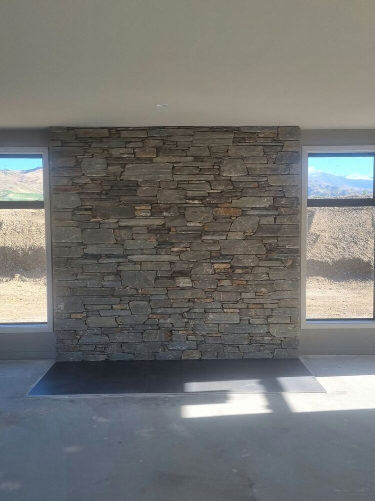 Garrett’s photo: a floor-to-ceiling schist feature wall in grey and rust tones, between two windows in a house under construction.